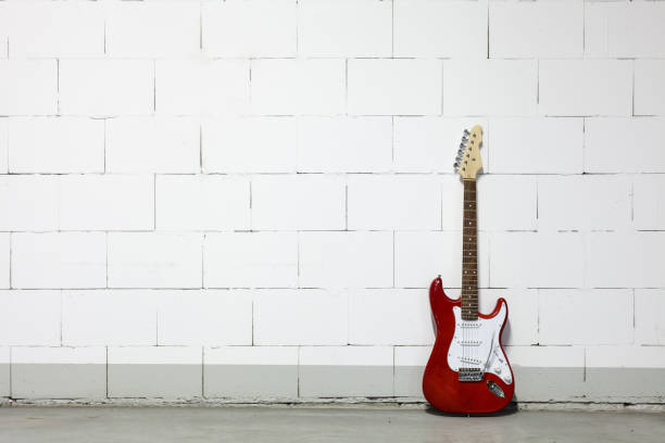 istock Red electric guitar stands to the right against white brick wall 1165518521