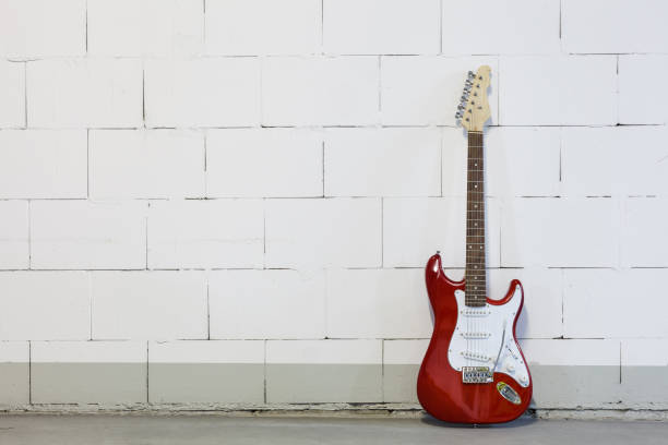 istock Red electric guitar stands to the right against white brick wall 1165518548