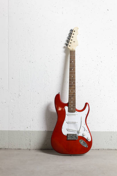 istock Red electric guitar standing against white raw wall 1165518590