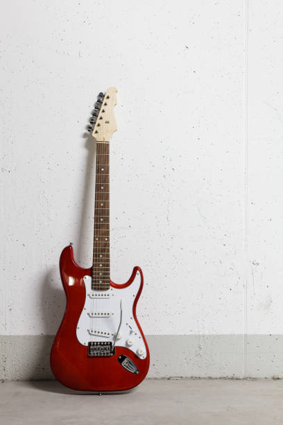 istock Red electric guitar standing left against white raw wall 1165518625