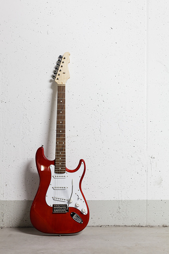 Red electric guitar standing left against white raw wall