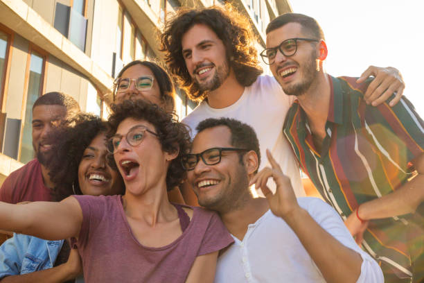 Funny curly haired woman in glasses taking selfie Funny curly haired woman in glasses taking selfie with her cheerful friends. Mix raced men and women grimacing and smiling at phone camera. Friendship concept group of people wearing eyeglasses stock pictures, royalty-free photos & images