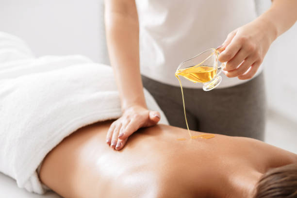 массажист наливает ароматное масло на женскую спину - masseur стоковые фото и изображения