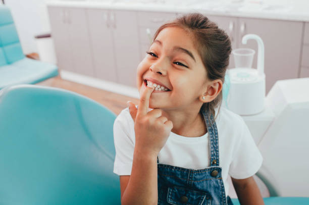 pequeña paciente raza mixta mostrando su sonrisa de nita perfecta mientras se sienta silla de dentistas - clinica dental fotografías e imágenes de stock