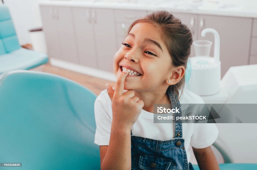 Mixed race little patient showing her perfect toothy smile while sitting dentists chair Child Stock Photo