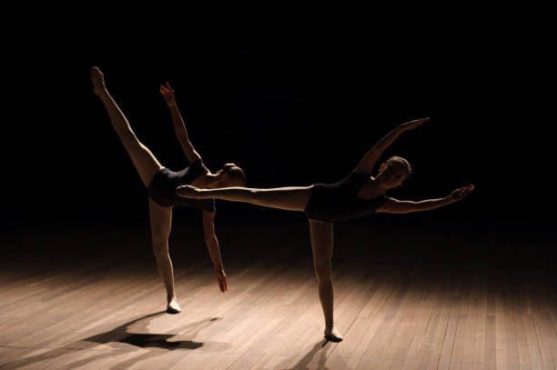 istock Flexible ballerinas stretch on a dark lighted scene 1165528319