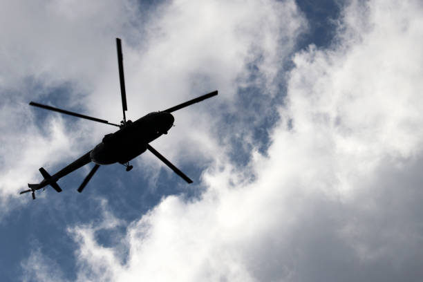 istock Helicopter silhouette in flight on background of blue sky with white clouds 1165533801
