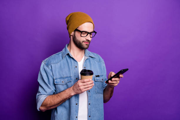 istock Cool handsome guy holding telephone drinking coffee casual outfit isolated violet background 1165538091