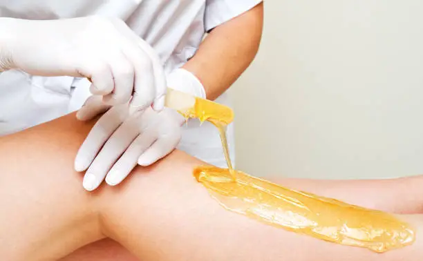 Photo of Cosmetologist beautician waxing female legs in the spa center beauty salon