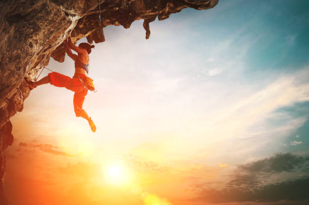 istock Athletic Woman climbing on overhanging cliff rock with sunset sky background 1165546697