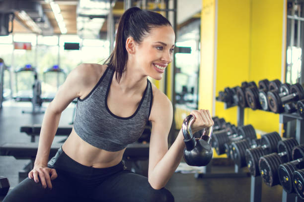 giovane donna in forma seduta sulla panchina dell'esercizio e campana del bollitore di sollevamento in palestra - picking up weight women sport foto e immagini stock