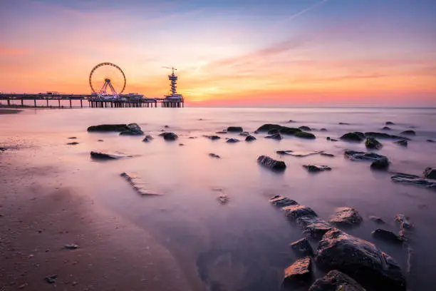 Photo of Colorful sunset on coastline, beach, pier and ferris wheel, Scheveningen, the Hague.