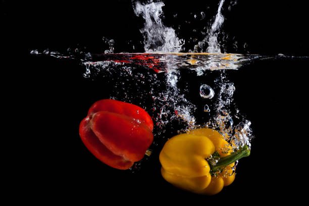 istock Yellow and red pepper falling into water and splashing against black 1165555051