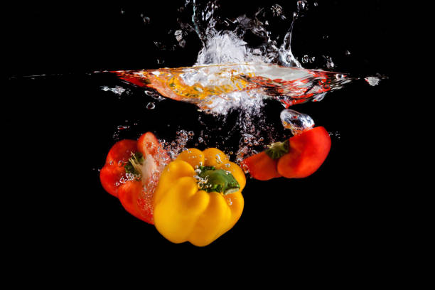 istock Yellow and red pepper falling into water and splashing against black 1165555052