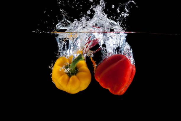 istock Yellow and red pepper falling into water and splashing against black 1165555169