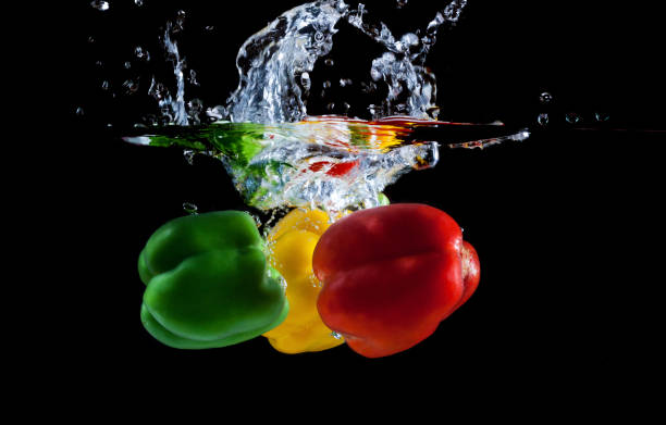 istock Yellow, green and red pepper falling into water and splashing against black 1165555172
