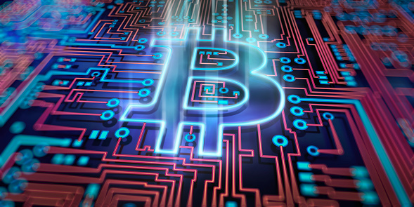 A conceptual image to represent cryptocurrency and blockchain currency. A glowing bitcoin symbol is depicted as part of a printed circuit board. With shallow depth of field, focussed on the centre of image. WIth a red and blue colour theme.