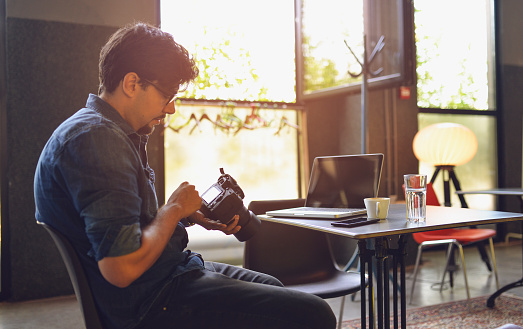 Hipster young man holding a DSLR camera and checking settings in his office