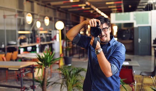 Young man using DSLR camera ,Hipster holding a DSLR camera in caffe