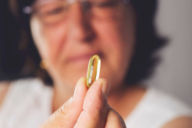 fish oil pill in old woman's hand on blurred background - fish oil cod liver oil doctor holding imagens e fotografias de stock