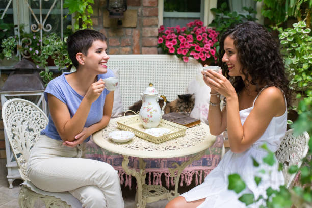 Indoor over shoulder shot of happy, cool, multiracial group of late teen Asian female friends gossiping and having fun together while enjoying coffee break with snacks and giving toothy smile. Three people horizontal composition with selective focus.