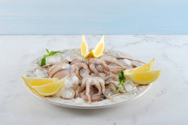 istock Raw mini octopus on a plate with ice. Mini octopuses are decorated with lemon wedges and basil leaves. 1165564711
