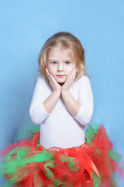 kleine mädchen ballerina in bunten tutu portrait. blonde kind in hübschen ballett rock auf neutral studio hintergrund. süße schüchterne modell posiert mit händen auf gesicht. entzückende kaukasische kid dancer im kostüm - ballet dress studio shot costume stock-fotos und bilder