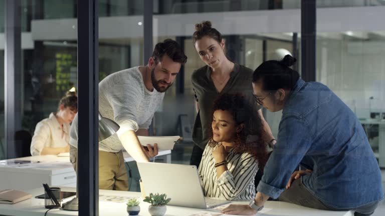 4k video footage of a group of young businesspeople using a laptop during a late night at work