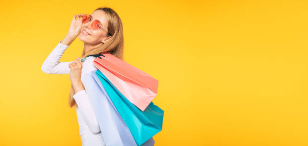 Happy customer portrait on yellow background. Purchases in hands. Shopping concept. Woman with shopping bags Happy customer portrait on yellow background. Purchases in hands. Shopping concept. Woman with shopping bags young women shopping stock pictures, royalty-free photos & images