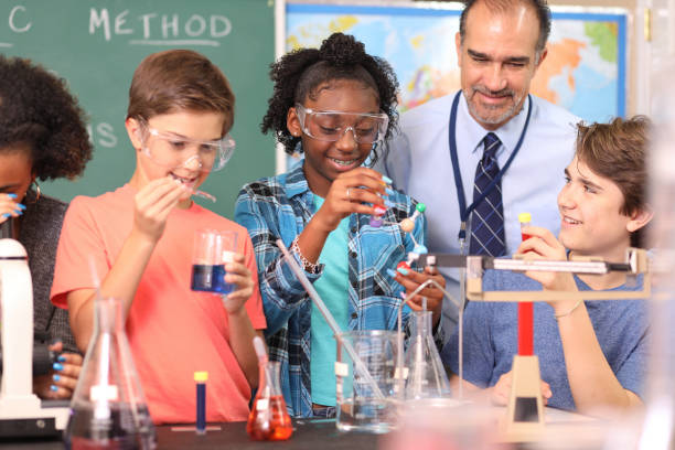 Junior high age school students conduct science experiments in classroom. Junior high, high school age students work on science experiments in school classroom setting.  STEM topics.  Laboratory glassware, microscope. high school high school student science multi ethnic group stock pictures, royalty-free photos & images