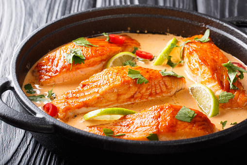 Fillet salmon in spicy Thai coconut sauce with lime and herbs close-up in a pan on the table. horizontal