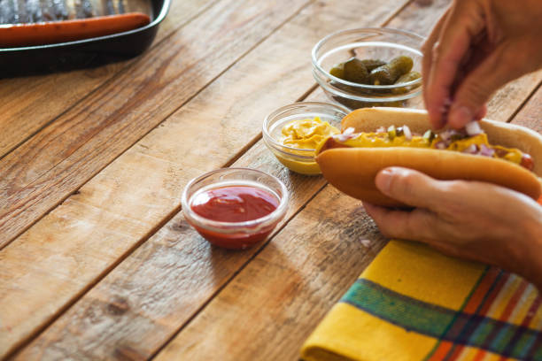 istock Hot dog preparing, adding chopped red onions and pickled cucumbers, close-up, motion blur 1165570716