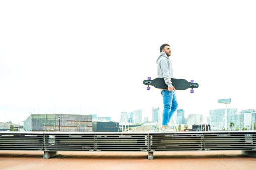 Casual man carrying longboard with Barcelona skyline at background