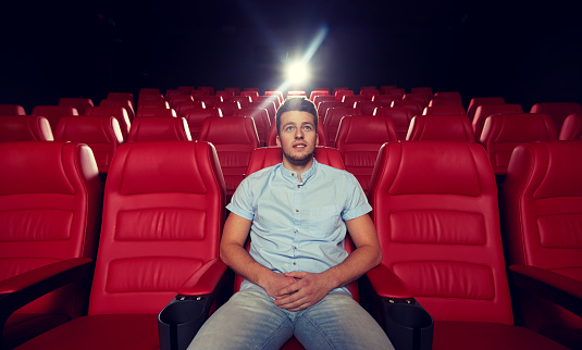 cinema, entertainment and people concept - happy young man watching movie alone in empty theater auditorium