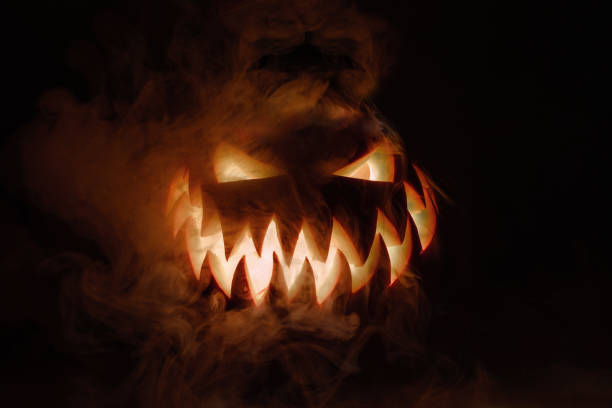 Fuming bright Jack-o'-lantern pumpkin on dark solid background. Glowing eyes and a terrible grin. Halloween minimal concept. Copy space. Desktop wallpapers Fuming bright Jack-o'-lantern pumpkin on dark solid background. Glowing eyes and a terrible grin. Halloween minimal concept. Copy space. Desktop wallpapers ominous photos stock pictures, royalty-free photos & images