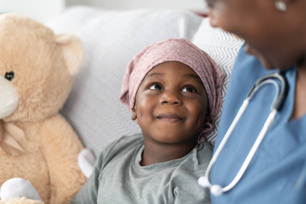 Smiling boy with cancer comforted by female doctor of African descent A young boy of African descent is at a medical consultation. He is dressed in casual clothes while wearing a headscarf to hide his hair loss. He sits beside his stuffed animal while listening to his doctor of African descent and smiling up at her. cancer illness stock pictures, royalty-free photos & images