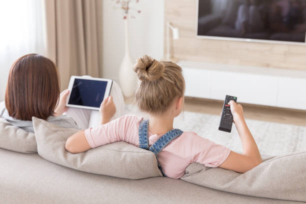 Mother And Daughter Sitting On Couch Watching Tv In Living Room Stock Photo  - Download Image Now - iStock