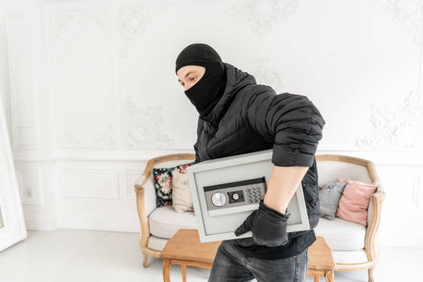 the burglar commits a crime in luxury apartment with stucco. thief with black balaclava stealing modern electronic safe box. - night deposit box imagens e fotografias de stock