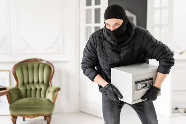 the burglar commits a crime in luxury apartment with stucco. thief with black balaclava stealing modern electronic safe box. - night deposit box imagens e fotografias de stock