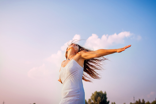 Young woman feeling free and happy raising arms and spinning around outdoors at sunset. Summer vacation