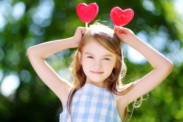 屋外で巨大なハート型のロリポップを食べるかわいい女の子 - child valentines day candy eating ストックフォトと画像