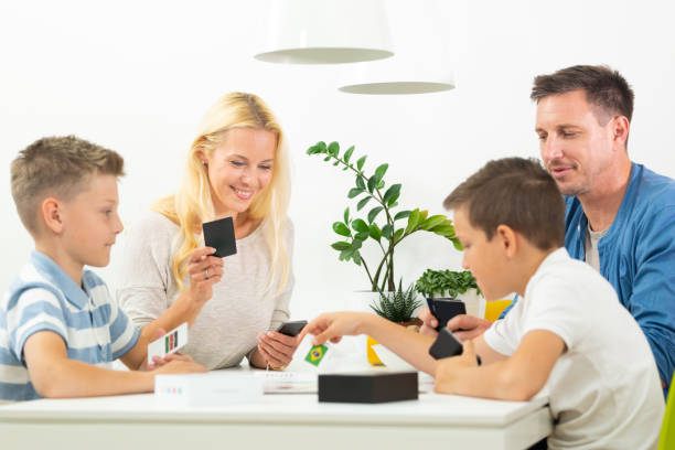 Happy young family playing card game at dining table at bright modern home. Happy young family playing card game at dining table at bright modern home. Spending quality leisure time with children and family concept. Cards are generic and debranded. family playing card game stock pictures, royalty-free photos & images