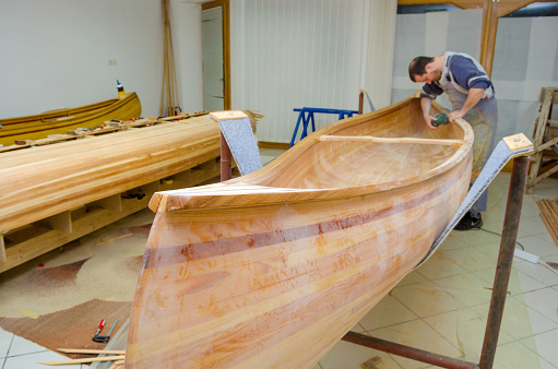 Young carpenter sandpapering wooden canoe of his own design.