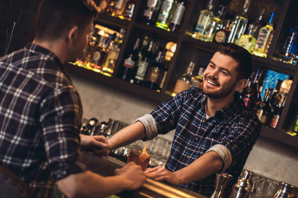 istock Young bartender standing at bar counter with customer talking happy 1165610896