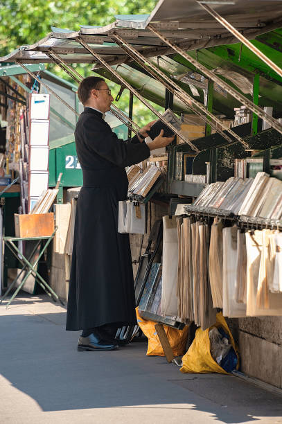 Priest at book stall along river Seine. Paris, France - July 04, 2017: A priest in cassock garment searches for a book at a pedestrian book stall by the river Seine. monsignor stock pictures, royalty-free photos & images