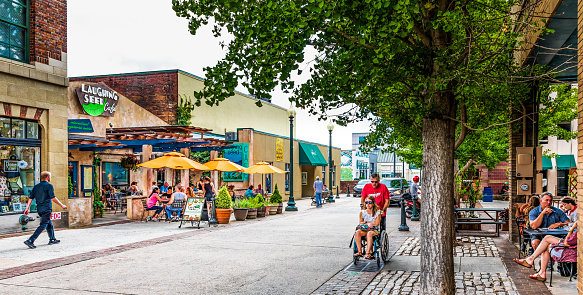 Asheville, NC, USA-27 July 2019: Wall Street in downtown is busy on a summer  Sunday, with small crowds at café tables, while a man pushes a young woman in a wheel chair.