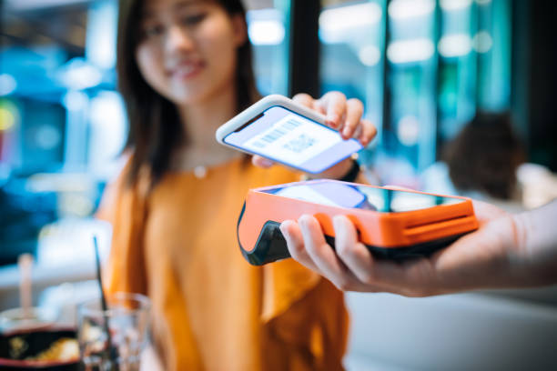 mujer joven asiática pagando con teléfono inteligente en un café. - pago por movil fotografías e imágenes de stock