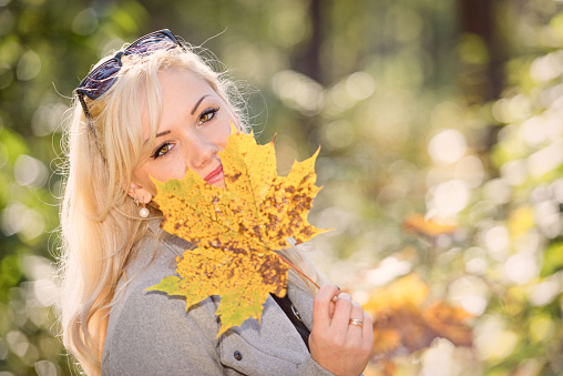 A young, blonde and smiling woman portrait on a sunny autumn day.