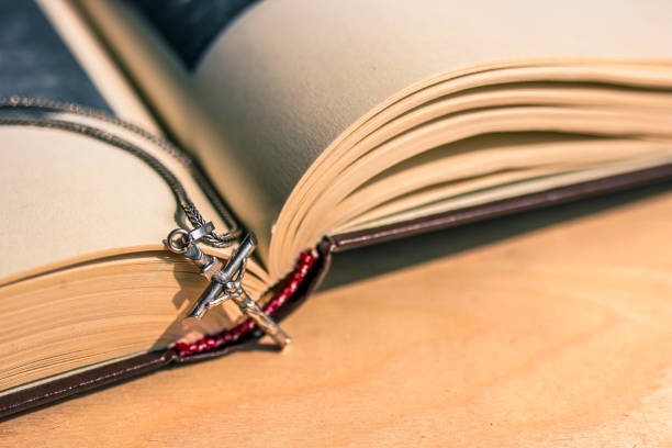 istock Open Bible book on wooden table and silver chain with silver cross close up view. 1165655901