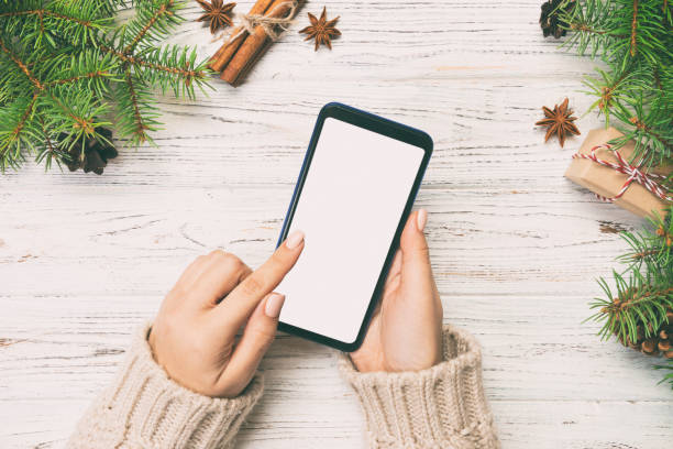 istock Christmas background: female hands messaging smartphone on rustic wooden table background with Christmas decoration. top view, flat lay. Toned 1165656280